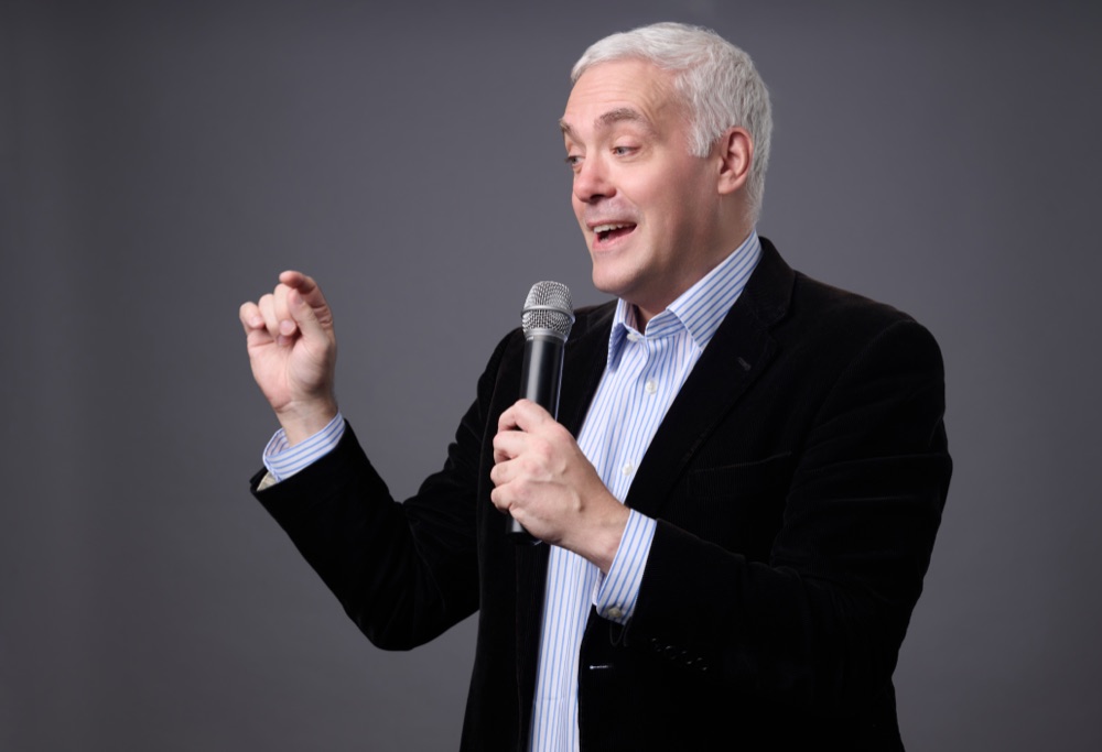 Ewan MacLeod speaking into a microphone against a grey studio background.