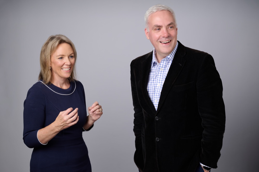 Holly Joint and Ewan MacLeod speaking together against a grey studio background.